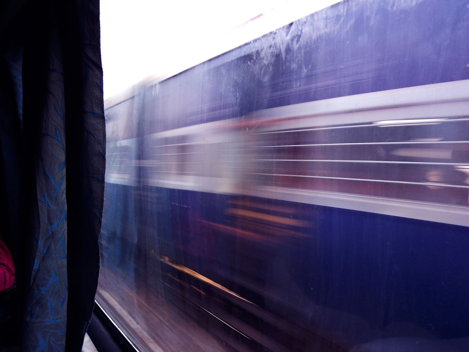 A Farbound.Net Photo showing a Rajdhani Express train speeding past another train. Visible from the window of an Ac 3 tire coach.