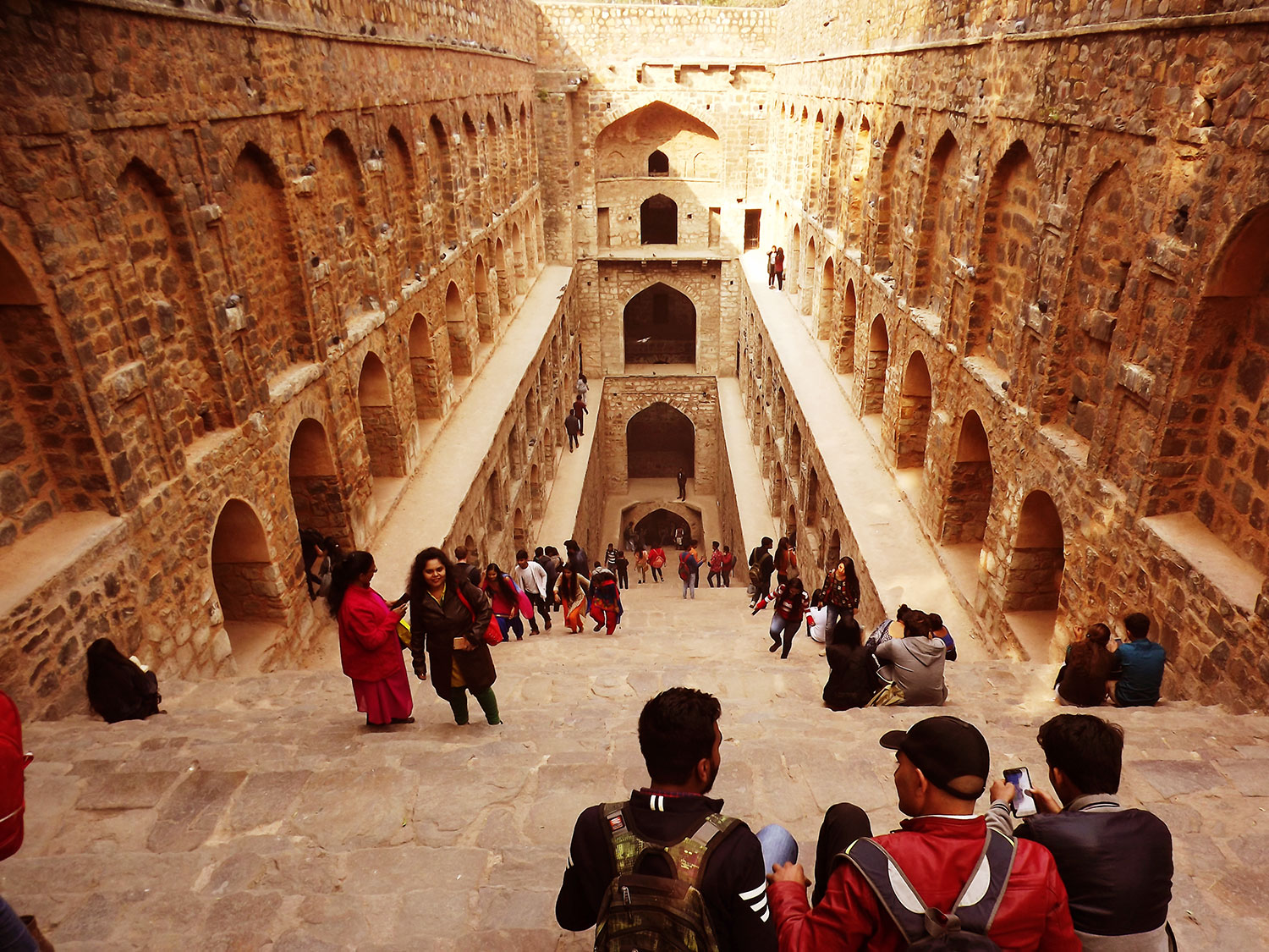 View of a flight of stone steps leading down inside the Ugersen Step well with visitors and tourists crowding the interior, Hailey's Road, near Connaught Place, New Delhi, India